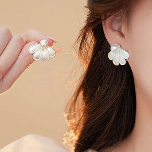 Macro view of shell-shaped silver stud earrings featuring a single white pearl on model