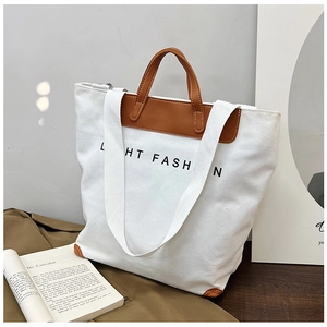 Detail view of white canvas tote bag with brown leather trim and handle on studio background