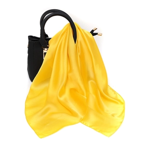 Detail of bright yellow satin scarf tied on a black leather handbag handle for style