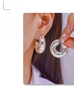 Detailed close-up of chunky silver C-shaped earrings with a polished mirror finish on model