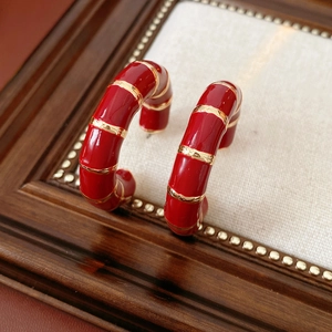 Detail of red enamel C-shape hoop earrings with gold bamboo design on vintage wood frame