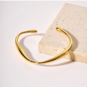 Close-up of golden irregular wavy cuff bracelet on textured travertine stone surface