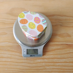 Detailed view of an Easter tin box being weighed on a digital scale at 70.9 grams