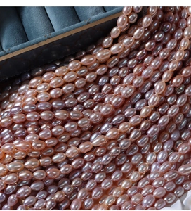 Macro shot of 5-6mm pink and purple freshwater rice pearls spilling from a blue velvet box