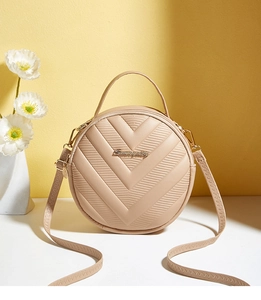 Detailed close-up of light brown round bag with elegant V-shaped quilted texture and metal logo