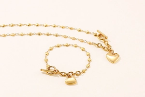 Detail of gold heart link necklace and bracelet set with toggle clasp on a clean background