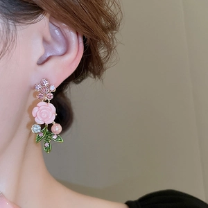 Close-up of floral earring with pink rose petals, green leaves, and white pearl accent