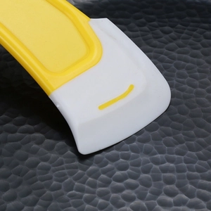 Silicone kitchen scraper with yellow handle cleaning food residue from a dark pot surface