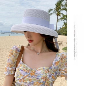 Detail of a white wide-brim straw hat featuring a purple bow ribbon against a beach backdrop