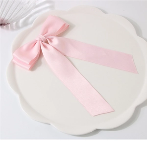 Detail of pink satin double-layered bow hair clip on a white petal plate with glass accessory