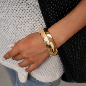 Dettaglio di un grosso bracciale geometrico dorato indossato con maglione bianco