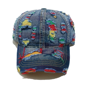 Dettaglio del cappello da baseball in denim invecchiato con fori e toppe colorate