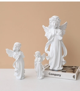 Three white resin praying angel figurines in a tiered arrangement on a warm background