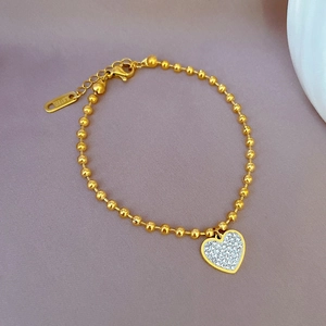 Detailed close-up of a gold stainless steel beaded bracelet with a sparkling crystal heart charm