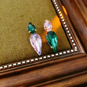 Close-up of teardrop-shaped green and purple zircon earrings on a vintage wooden frame