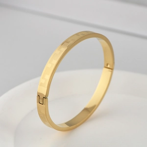 Detail of gold titanium steel bangle with geometric engraved pattern and clasp closure