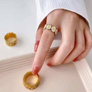 Detail of wide gold mahjong theme rings and white enamel daisy ring on a ceramic tray