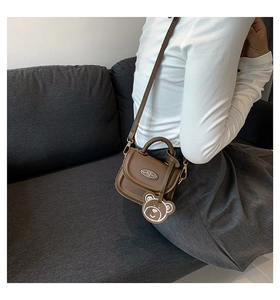 Brown mini crossbody bag with cute bear charm shown in a natural lifestyle setting