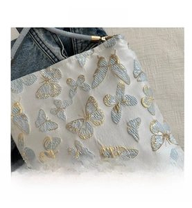 Macro view of blue butterfly floral embroidery on a white fabric shoulder bag surface