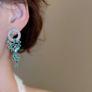 Détail de boucles d'oreilles pendantes en argent avec zircons verts portées par un mannequin