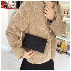 Detail of black suede envelope bag with elegant gold chain strap worn on shoulder