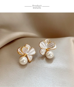 Gros plan de boucles d'oreilles fleurs et perles dorées sur un fond de soie couleur champagne