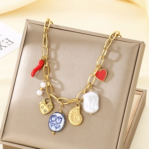 Detail of gold multi-charm necklace with pearls, chili, and heart on beige satin