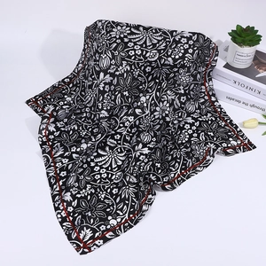 Detail of a square silk scarf with black floral paisley print and elegant red border