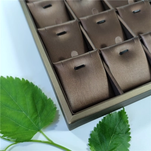Detail view of a 24-slot jewelry display tray with brown satin cushions and green leaf accents