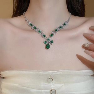 Detail of silver necklace with green water drop pendant and small diamonds on a model