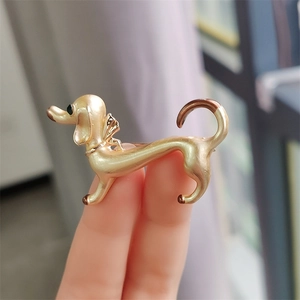 Detail of creative dachshund dog brooch in gold plating held by fingers for scale