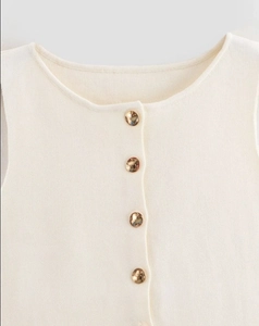 Détail du haut en tricot sans manches blanc cassé avec boutons dorés sur le devant