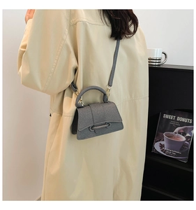 Gros plan d'un sac bandoulière gris en tissu texturé avec poignée et base incurvée