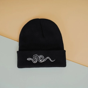 Close-up of white snake embroidery detail on a black knit beanie with clear texture