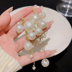 Elegant cluster of dangling faux pearls with gold chains held by hand against a white plate