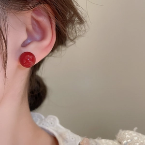 Close-up of a model wearing a glossy red spherical stud earring with gold plating