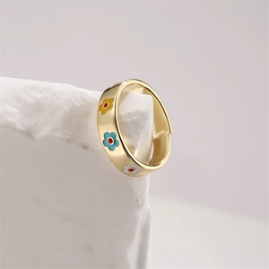 Detail of gold ring with colorful enamel flowers on white textured stone background