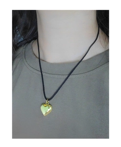 Detail of a gold heart pendant with black cord necklace worn on a female neck