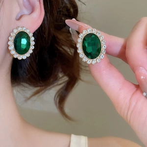 Detail of vintage gold stud earrings with oval green gemstone and crystal halo on ear