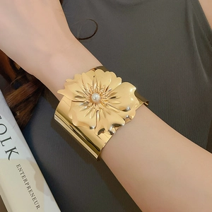 Detailed view of wide gold cuff bracelet featuring a large flower with pearl center