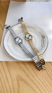 Detailed view of square dial gold and silver chain watches on a decorative white porcelain plate