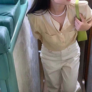 Chic model wearing a vintage pearl necklace paired with a beige short-sleeved shirt