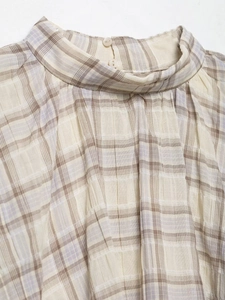 Detail of plaid high neck top featuring ruffled collar and double back button closure