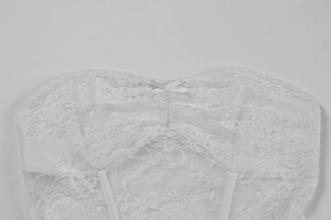 Detail of white lace tube top with floral patterns and a small ribbon bow on front