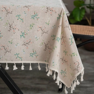 Close-up of beige cotton linen tablecloth with floral patterns and elegant tassel detail