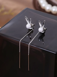 Macro shot of silver bunny-shaped pearl drop long chain earrings on dark surface
