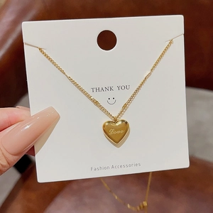 Detail of gold heart pendant with Love engraving on a white display card