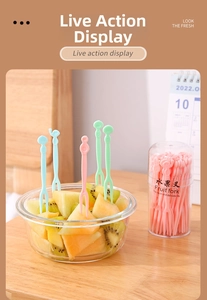 Close-up of colorful macaque plastic fruit forks in a glass bowl with fresh kiwi slices