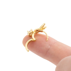 Golden cartilage huggie earring with zircon leaf charm held between fingers on white background