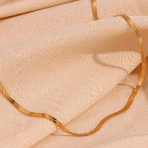 Detailed macro view of a 2mm gold-plated stainless steel flat snake chain on fabric